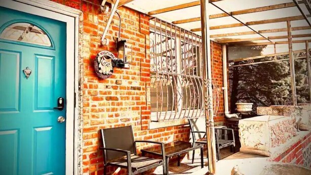 A room with a blue door, a brick wall, a window with metal bars, and a bench.