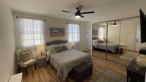 A bedroom with a bed, bedside tables, a mirror, a ceiling fan, and a view of the outside through the window. - San Diego Old Town Family-sized Apartment with Patio (San Diego)
