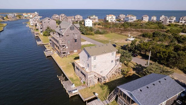 An aerial view of a coastal residential area with houses along a waterway, featuring a prominent stone building with a tower and a large house with a balcony. - 7557-Turtle's Pace - Avon Canalfront Retreat With Private Dock (Avon)