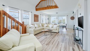 A spacious living room with a wooden staircase, a beige sectional sofa, a dining area, and a TV on a black stand. - 7557-Turtle's Pace - Avon Canalfront Retreat With Private Dock (Avon)