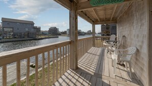 A wooden deck with a railing overlooking a body of water, with buildings in the background. - 7557-Turtle's Pace - Avon Canalfront Retreat With Private Dock (Avon)