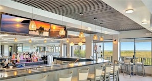 A modern bar area with a long counter, multiple hanging light fixtures, and large windows offering a view of the outdoors. - CP 223 Ocean View Condo - Vacation Rental in Ocean Village (Fort Pierce)