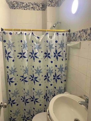 Een badkamer met een douchegordijn met een blauw bloemenpatroon, een witte wastafel en een spiegel boven de wastafel.