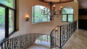 A spacious interior with a high ceiling, large windows, and a curved staircase with ornate railings. - Stunning Ocean View Chateau - Experience it All (Playa Hermosa, Sardinal)