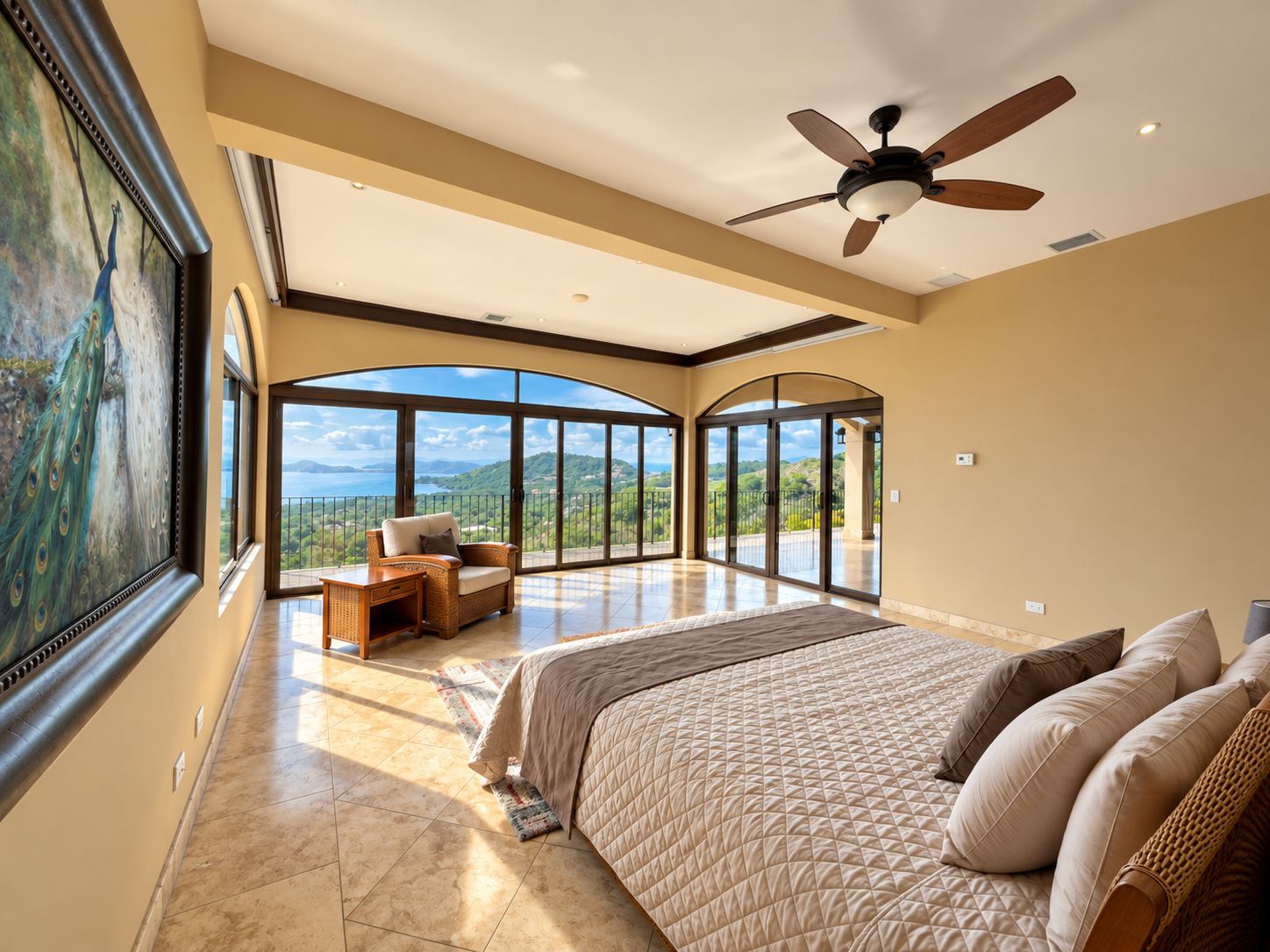 A spacious bedroom with a large bed, a ceiling fan, and a view of the outdoors through large windows.