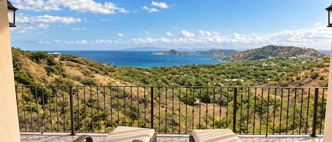 A balcony with two lounge chairs, a view of a coastal landscape, and a clear sky.