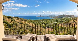 A balcony with two lounge chairs, a view of a coastal landscape, and a clear sky.