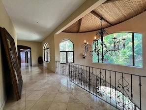 Stunning corridor with polished tile floor, ornate chandelier, and decorative wrought iron railing.