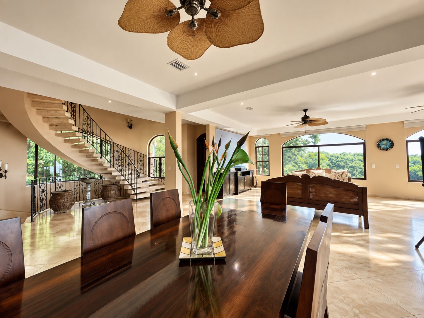 A spacious living area with a large wooden dining table, a staircase, and a view of the outdoors.
