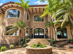 A multi-story house with a stone facade, large arched windows, and a central circular stone feature.