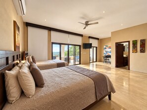 A spacious bedroom with two beds, a ceiling fan, and a view to the outside.