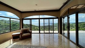 A spacious room with large windows offering a panoramic view of a lush landscape. - Stunning Ocean View Chateau - Experience it All (Playa Hermosa, Sardinal)