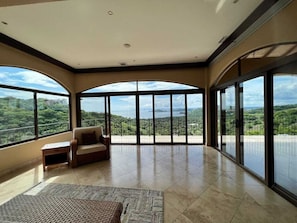 Enjoy expansive views of the lush landscape from the large windows in this room, which features a comfortable seating area and a tiled floor.