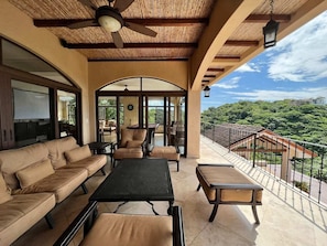 Relax in a spacious outdoor lounge with a long table, comfortable sofas, and armchairs, surrounded by a lush landscape.