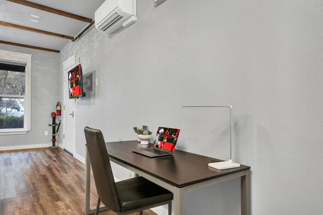 Un espace de bureau moderne avec un bureau en bois, une chaise, un ordinateur portable, une petite plante et un tableau encadré accroché au mur.