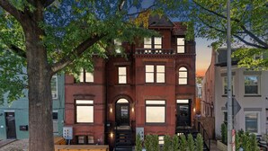 A two-story brick building with a prominent entrance, large windows, and a small porch area. - 8BR/7BA Mansion · Sleeps 28 · Shaw Metro (Washington)