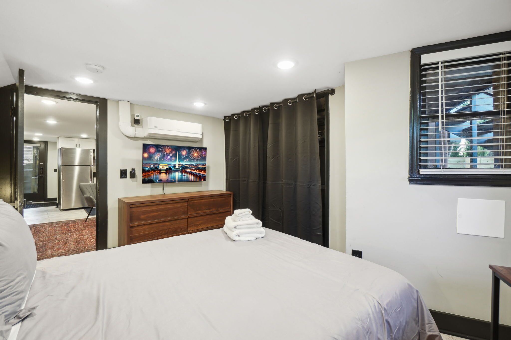 A hotel room with a bed, a wooden dresser, a TV, and a window with blinds.