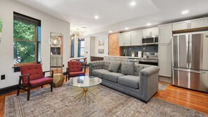 A modern kitchen with stainless steel appliances, a grey sofa, and a red armchair. - 8BR/7BA Mansion · Sleeps 28 · Shaw Metro (Washington)