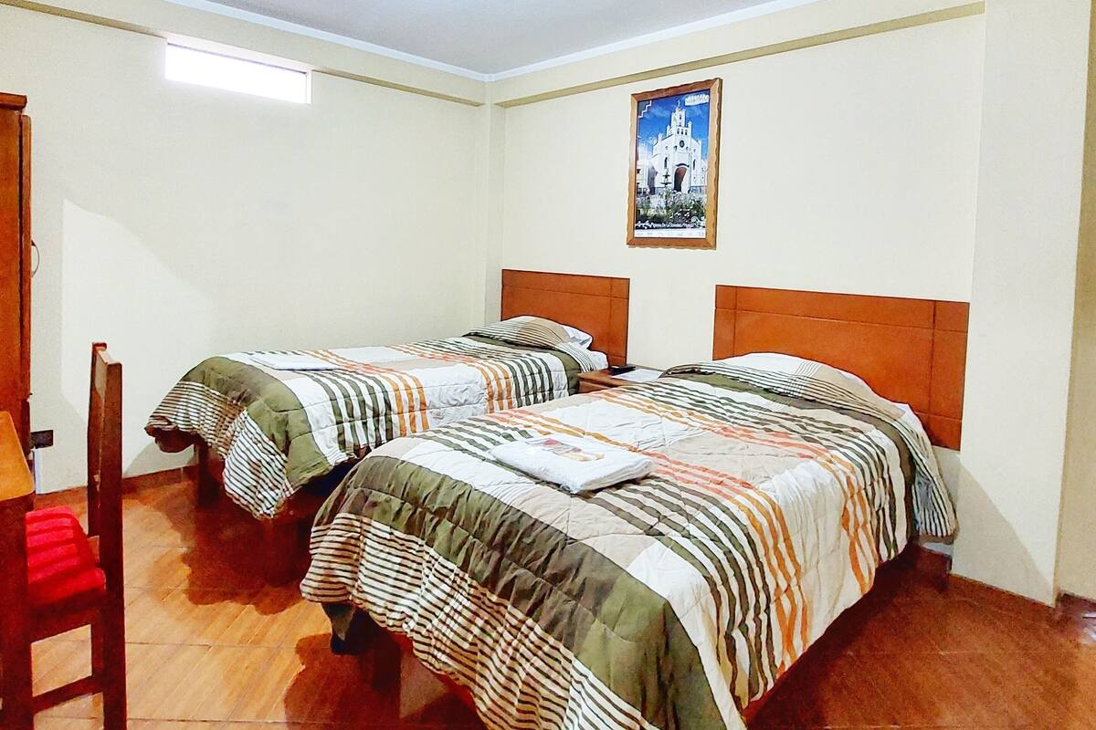 A room with two beds, a wooden chair, and a framed picture on the wall.