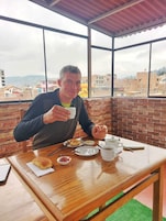 Una persona sentada a una mesa de madera con vistas a edificios a través de amplios ventanales.
