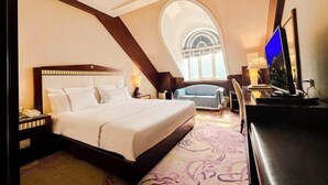 Una habitación de hotel con una cama grande, un escritorio con computadora, un televisor y vistas a la ciudad a través de una ventana.