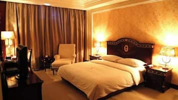 Ein Hotelzimmer mit einem großen Bett, einem Sessel, einem Schreibtisch und zwei Nachttischen mit Lampen.