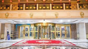 Un vestíbulo con alfombra roja, puerta giratoria de vidrio y techo decorativo.