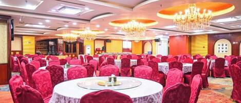 A banquet hall with round tables, red upholstered chairs, chandeliers, and a carpeted floor.