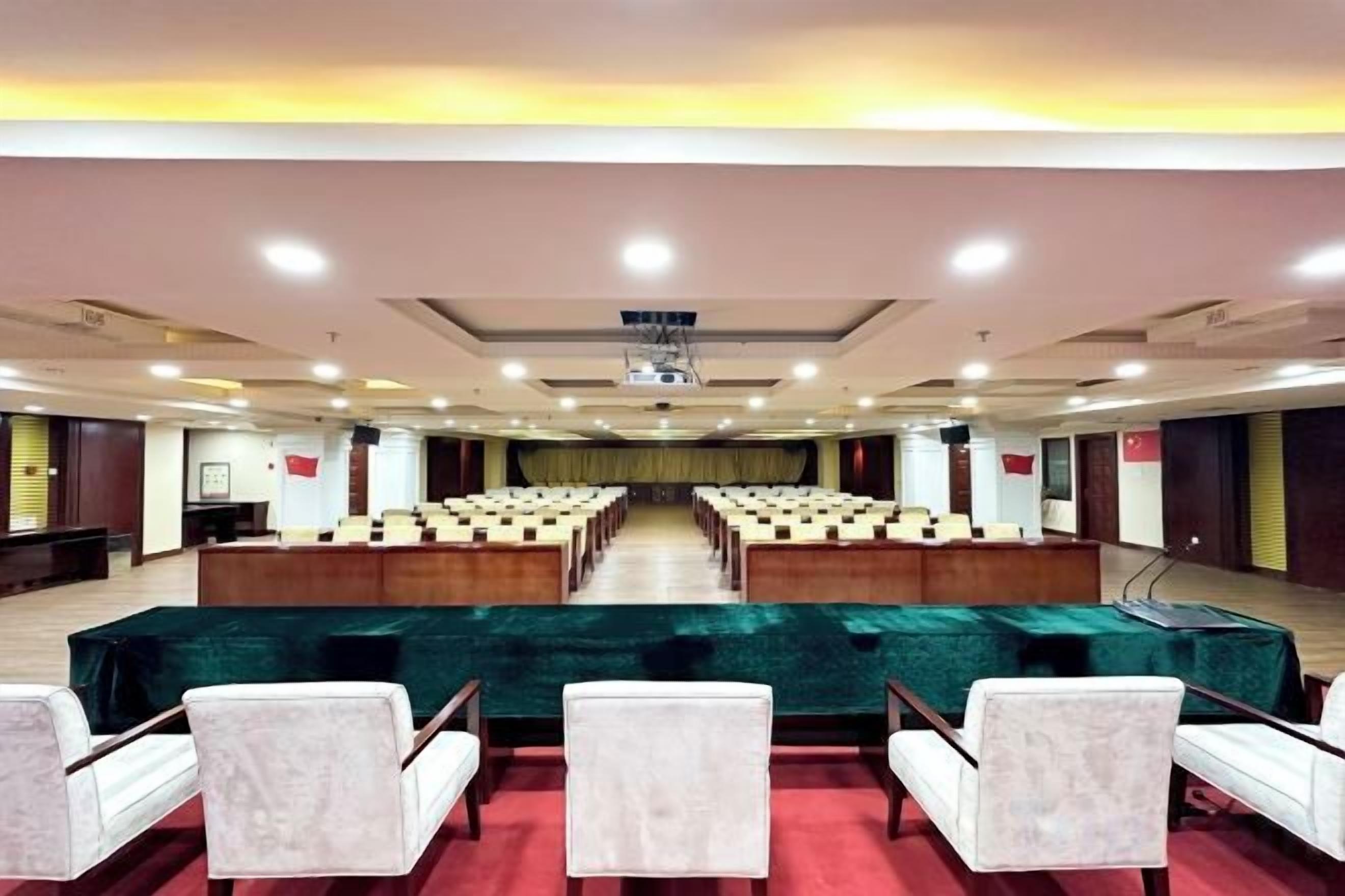 A conference room with rows of chairs, a stage, and a large screen.