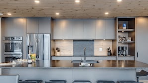 Eine moderne Küche mit einer zentralen Kochinsel, Barhocker, integrierten Geräten und einer Holzbeschichtung an der Decke.
