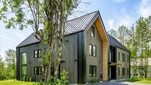 Ein modernes, zweistöckiges Haus mit geneigtem Dach, großen Fenstern und Holzfassade.