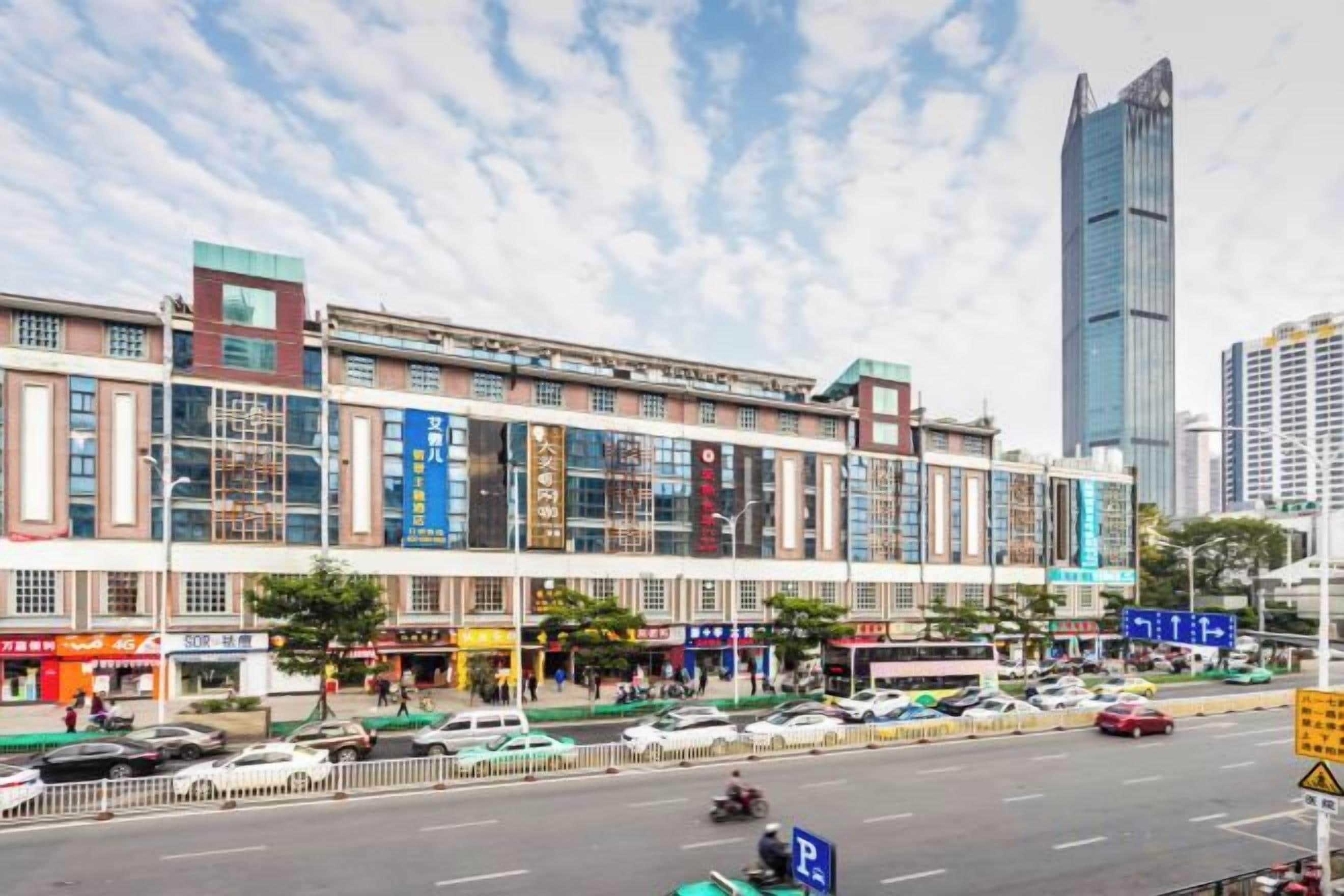 A multi-story building with commercial shops on the ground floor and a parking lot in front.