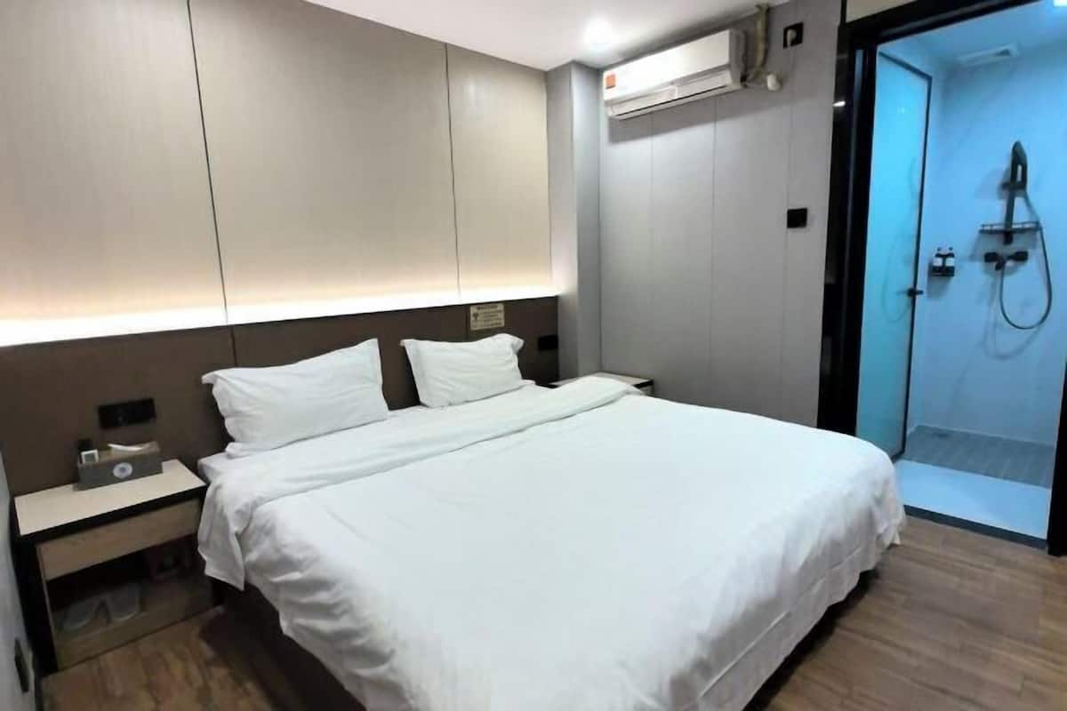 A modern hotel room with a bed, bedside table, and a shower area.