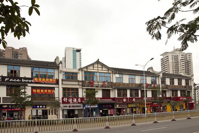 Una hilera de edificios comerciales con diferentes escaparates, incluyendo un letrero de Facebook, y una calle en medio.