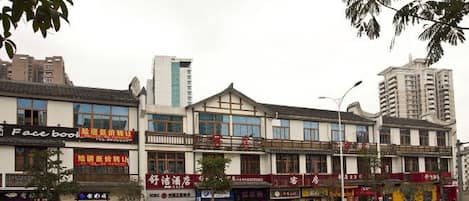 A row of commercial buildings with various storefronts, including a Facebook sign, and a street in between.