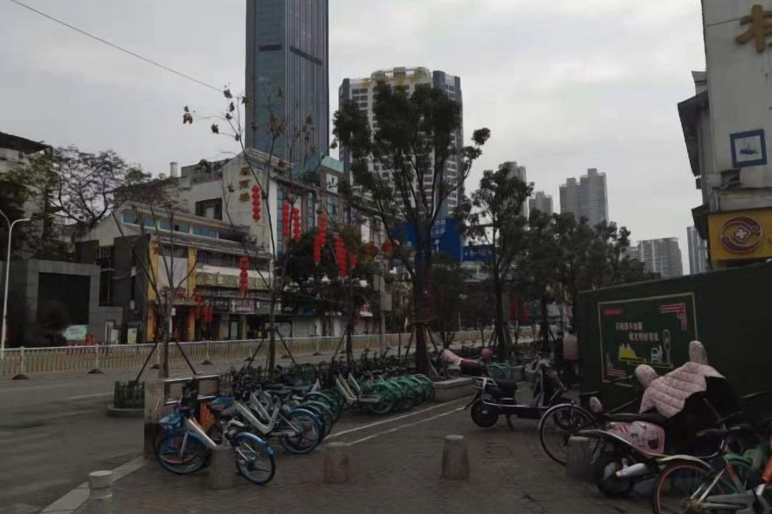 Una calle con bicicletas estacionadas a lo largo de la acera, un edificio con un cartel y una estructura alta al fondo.