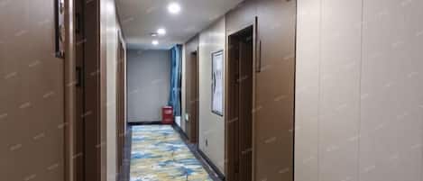 Un pasillo de hotel con puertas a ambos lados, una alfombra estampada y un extintor de incendios al fondo.