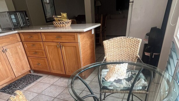 Un coin repas avec des chaises en osier et une table en verre, une cuisine avec des meubles en bois et un sol carrelé.