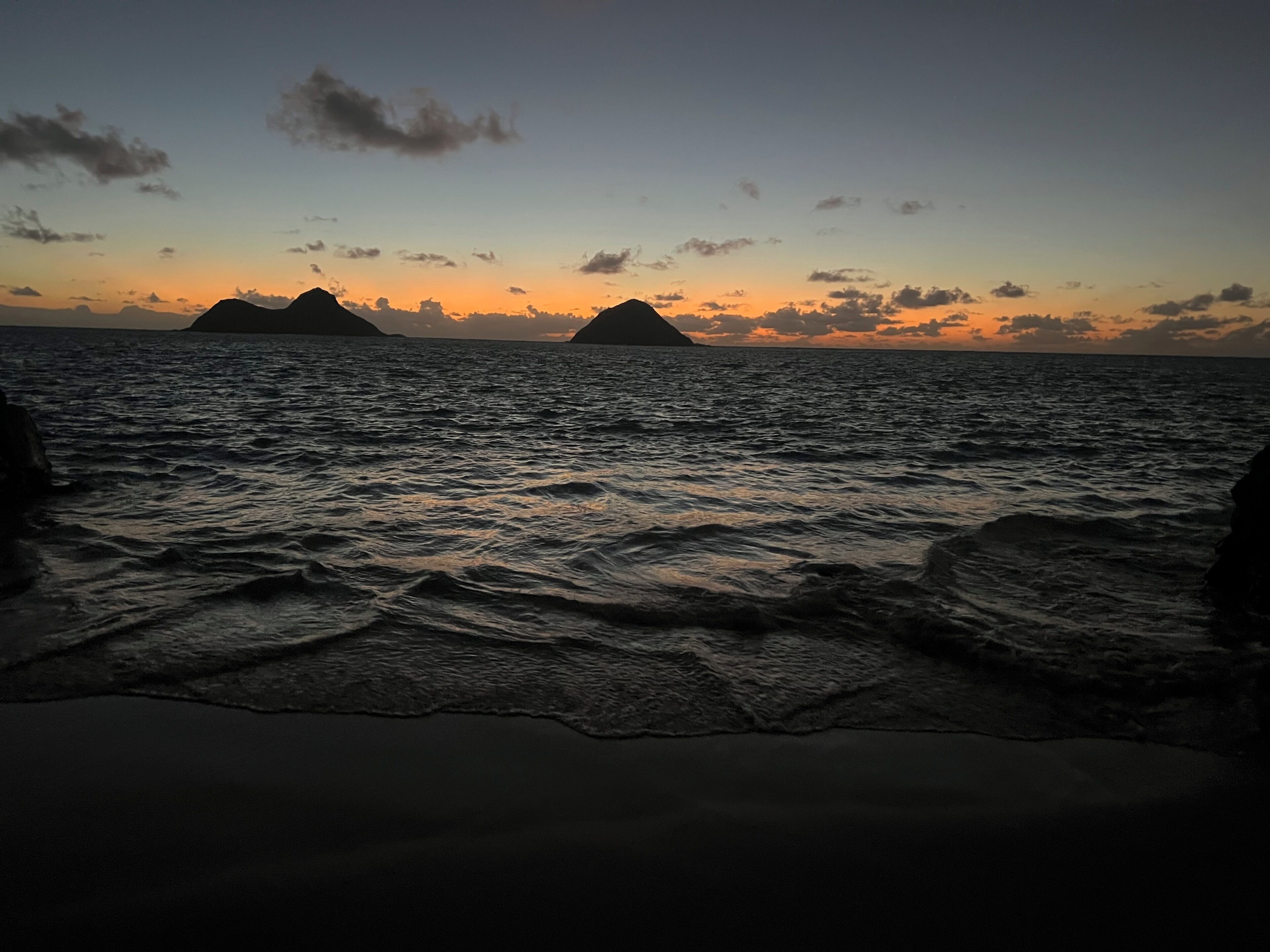 A beach with waves and distant islands during sunset.