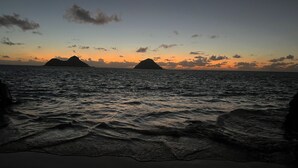 Une plage avec des vagues et des îles lointaines au coucher du soleil.