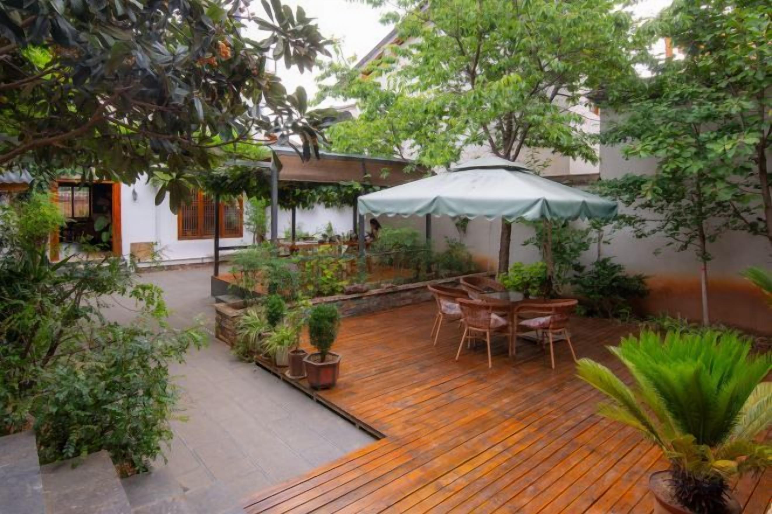 Terraza de madera con mobiliario exterior, rodeada de plantas en macetas y una zona de estar cubierta.