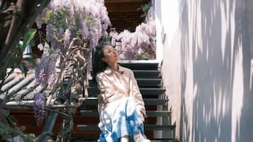 A person sitting on a staircase with a building and purple flowers in the background.