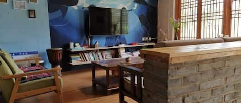 A living room with a large TV, wooden furniture, a bookshelf, and a mural of whales.
