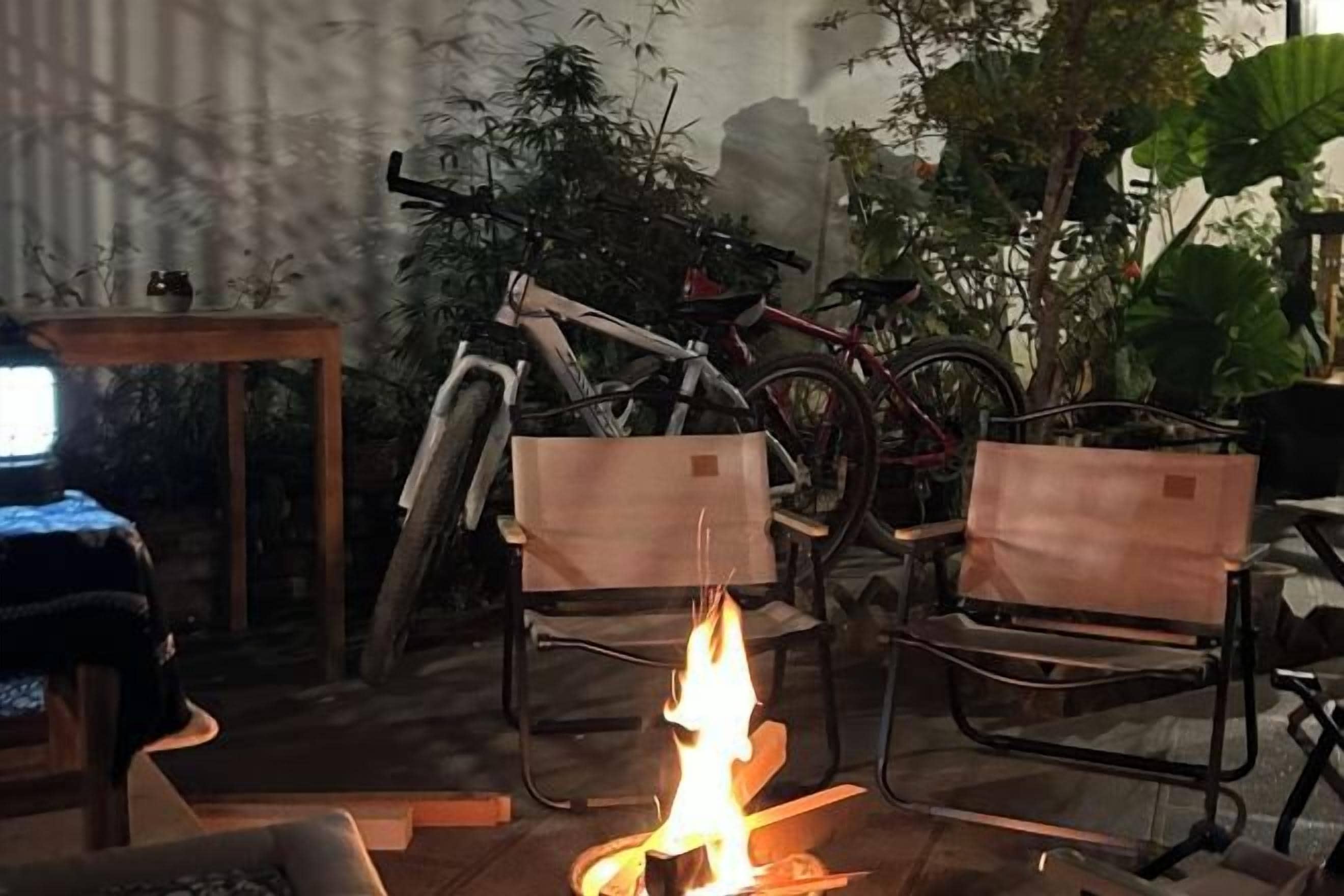 A room with a fire, two chairs, a table, and bicycles.