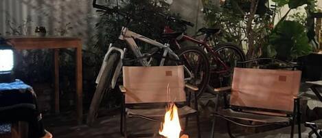 A room with a fire, two chairs, a table, and bicycles.