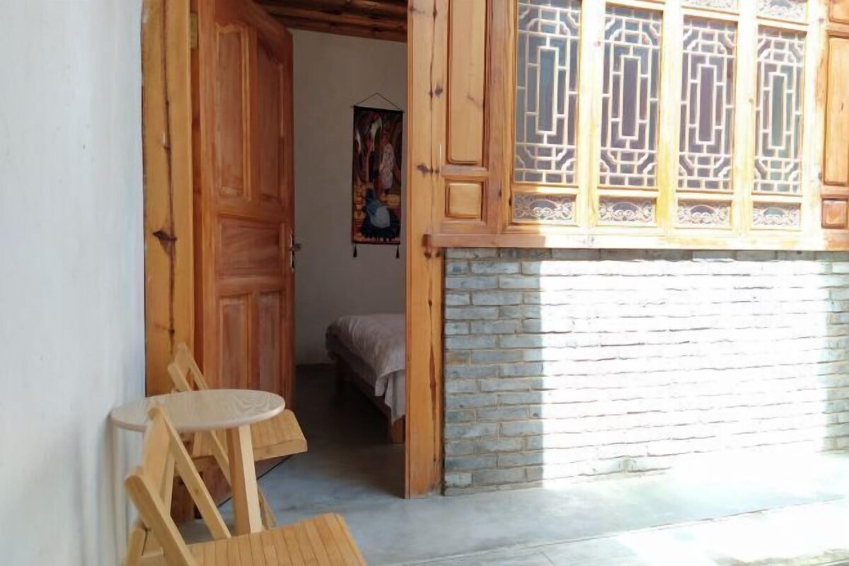 Una habitación con puerta de madera, una pequeña mesa redonda y una cama con manta.