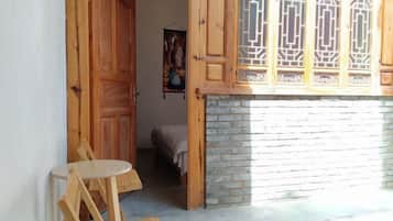 A room with a wooden door, a small round table, and a bed with a blanket.