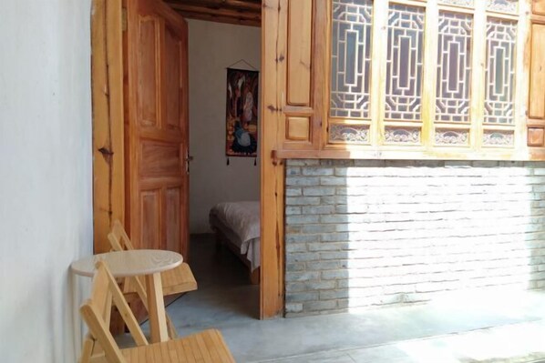 Una habitación con puerta de madera, una pequeña mesa redonda y una cama con manta.