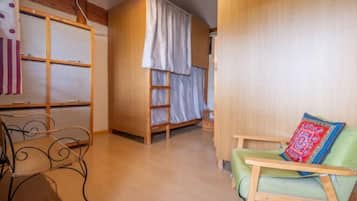 A cozy room with a bunk bed, a green armchair, a metal chair, and a wooden table.