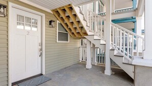 Una casa de dos pisos con fachada blanca, una puerta principal con un número y una escalera de madera.